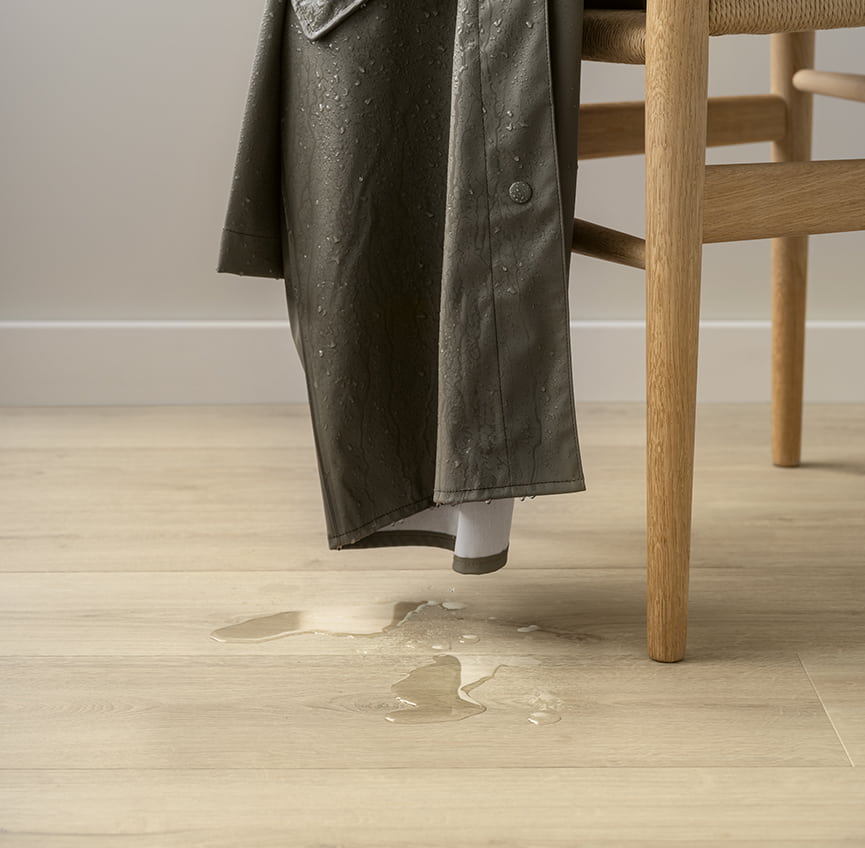 cappotto antipioggia appeso alla sedia con gocce d'acqua che cadono su un pavimento laminato beige